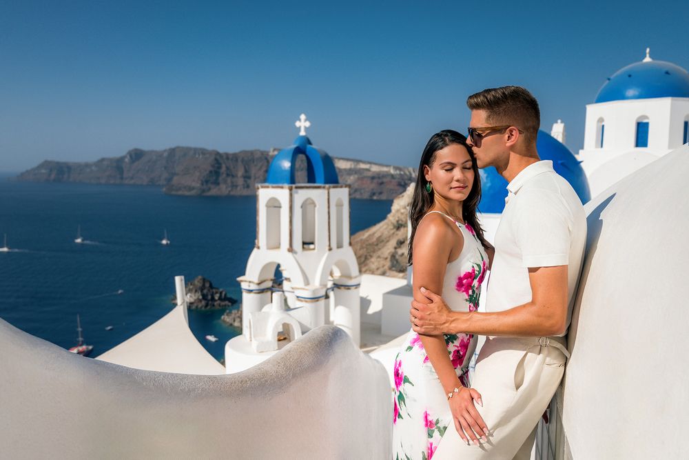 Romantic couple poses against iconic white domes and blue sea views of Santorini, Greece.