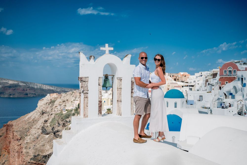 A couple enjoying the iconic white architecture and blue domes of Santorini, Greece with ocean views in the background.