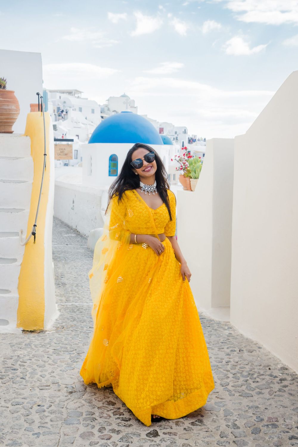 A bright yellow maxi dress stands out against the white buildings and blue dome of Santorini, Greece.