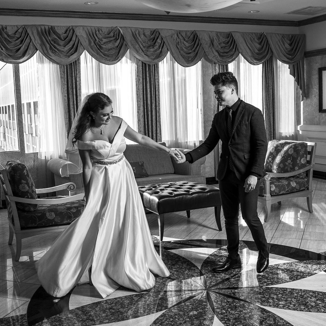 Black and white photo of bride and groom dancing in an elegant hotel lobby.