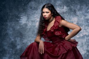 Woman in stunning red ruffled ball gown posing against blue-gray textured studio background.