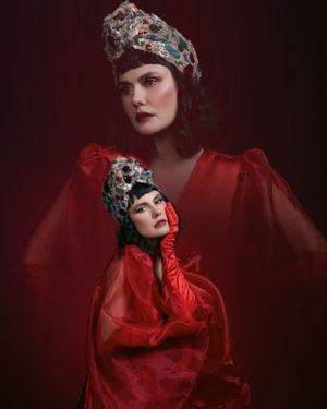 Two women in ornate jeweled headdresses and red silk garments in dramatic editorial fashion portrait.