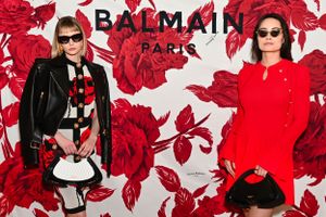 Two fashionable women posing at Balmain Paris event in front of red floral branded backdrop.