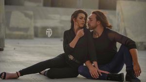 Couple dressed in black sitting closely together on a concrete floor in an urban setting.