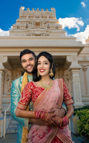 Indian couple in traditional wedding attire posing in front of a ornate Hindu temple on their wedding day.