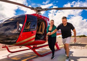 Excited couple running from a red helicopter during an adventurous scenic tour on a sunny day.