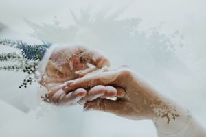 Close-up of bride and groom exchanging rings with delicate lace and floral details in soft light.