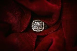Luxury diamond cluster engagement ring displayed on rich red velvet fabric background.