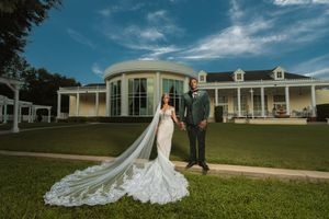 Bride in cathedral veil mermaid gown and groom in green suit posing before elegant estate venue.
