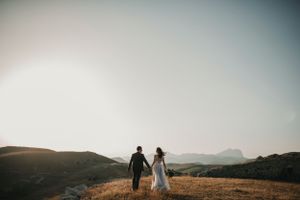 Bride and groom holding hands walking across golden hillside landscape at sunset during elopement.
