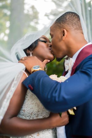 Newlyweds sharing a romantic kiss under a bridal veil outdoors.