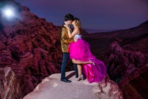 Couple sharing a romantic kiss on a rocky outcrop under a dramatic night sky in red canyon.