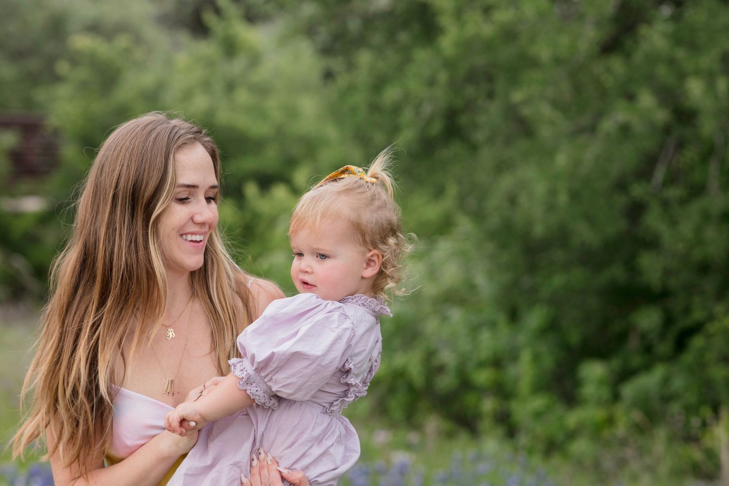 Mom and baby share a joyful moment together outdoors in the bluebonnets with lush greenery in the background.