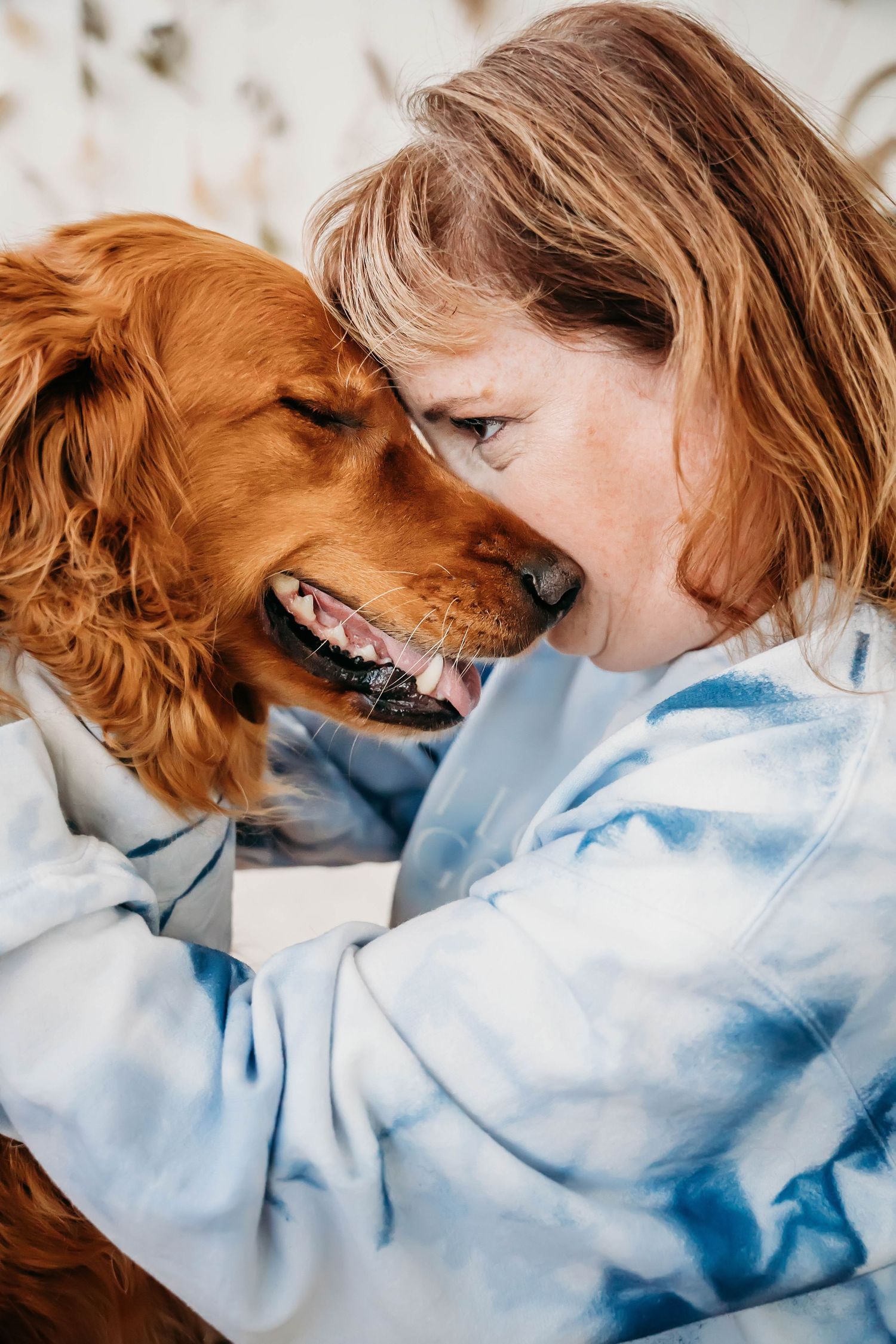 Golden retriever and person share an intimate bonding moment in soft lighting while wearing blue tie-dye clothing.
