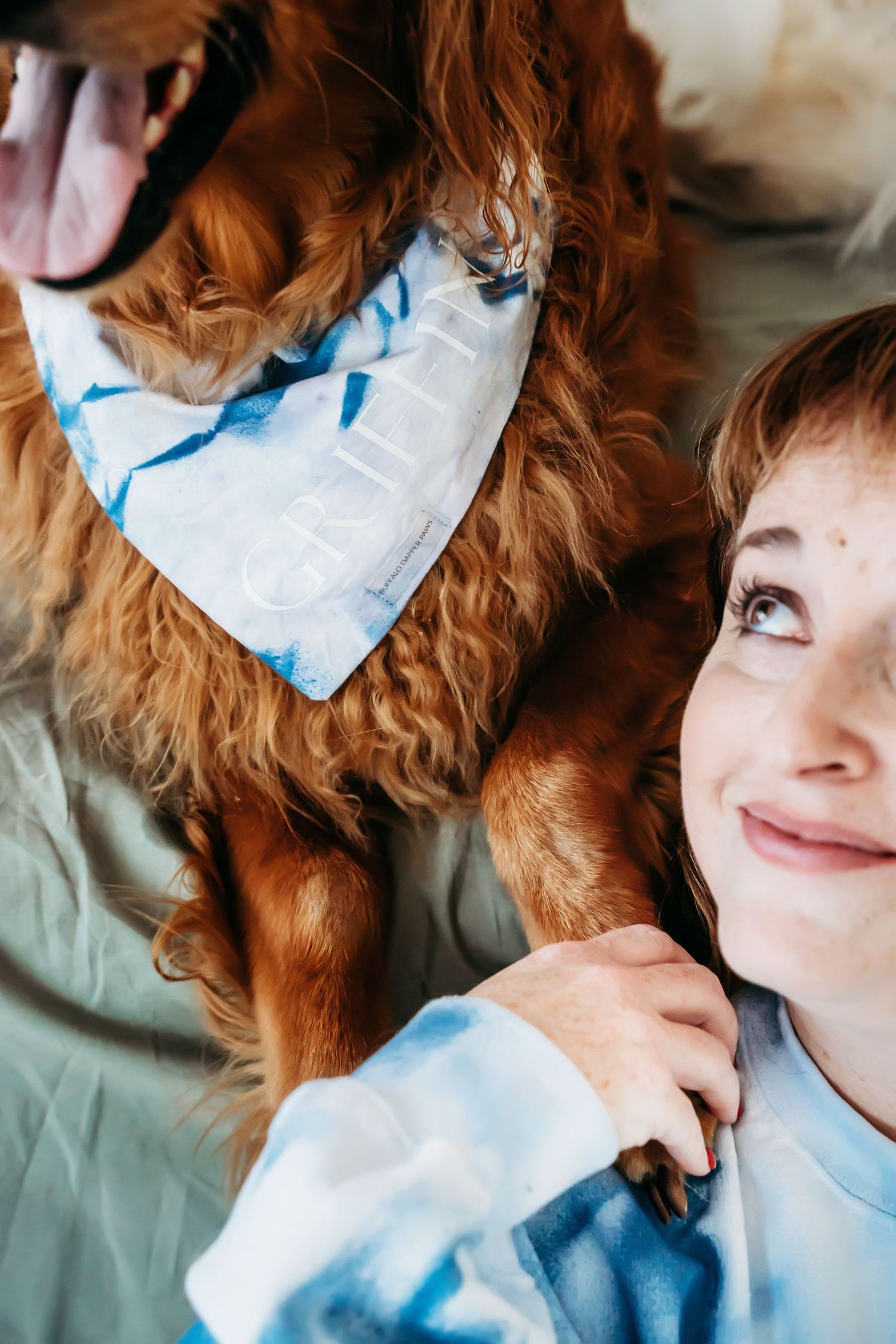 Sweet moment between golden retriever wearing blue bandana and companion in tie-dye sweatshirt.