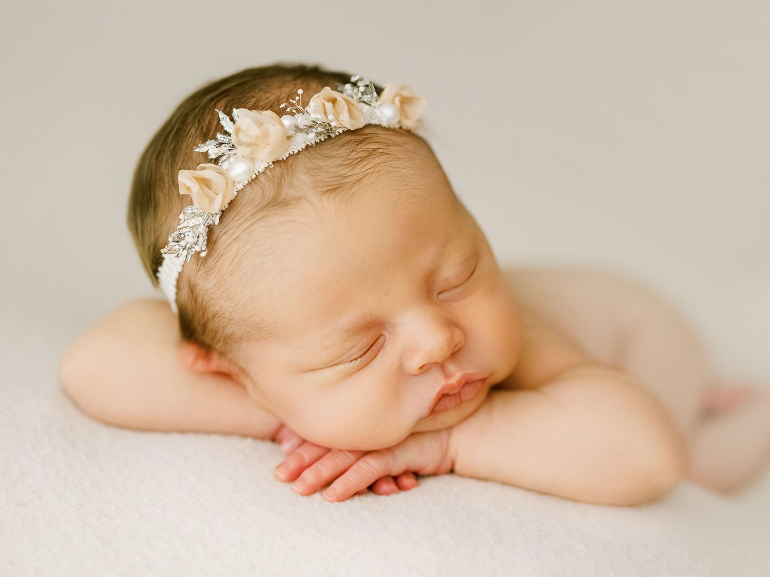Sleeping newborn wearing delicate lace headband during professional photography session.