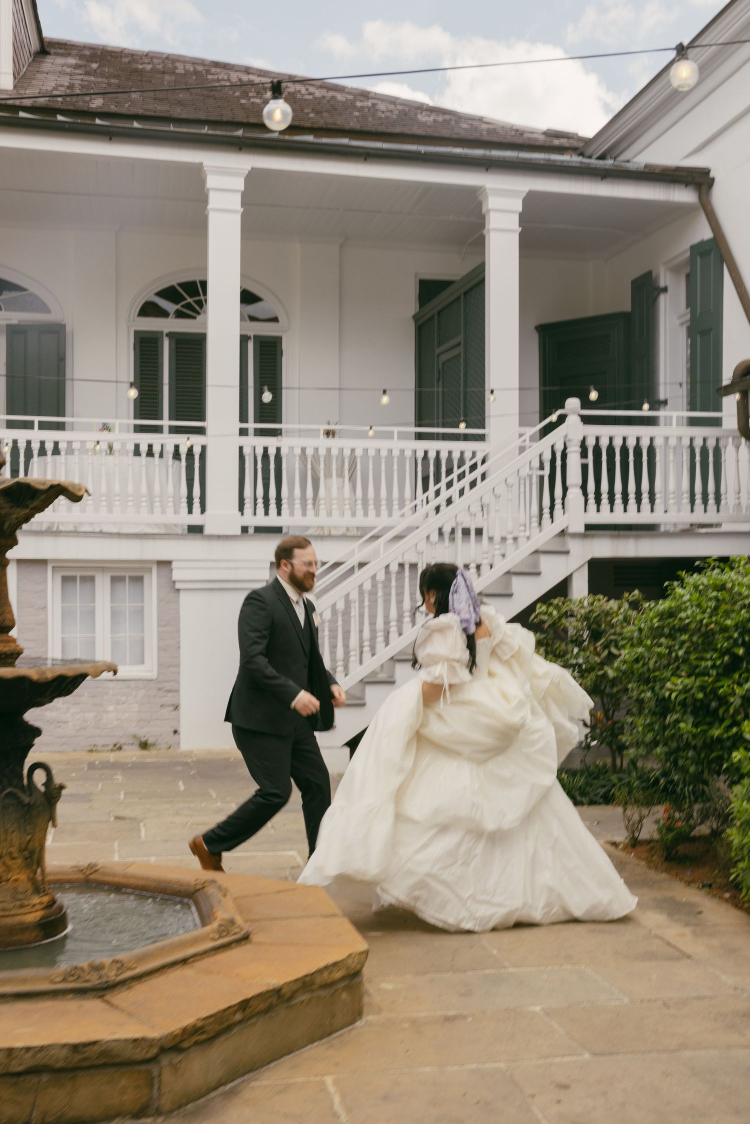A lively wedding celebration takes place on the lawn outside a white church with a steeple on a sunny day.