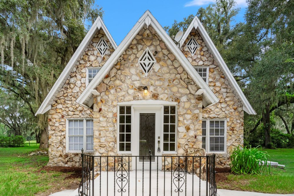 Charming stone cottage with white trim windows and gabled roof design.