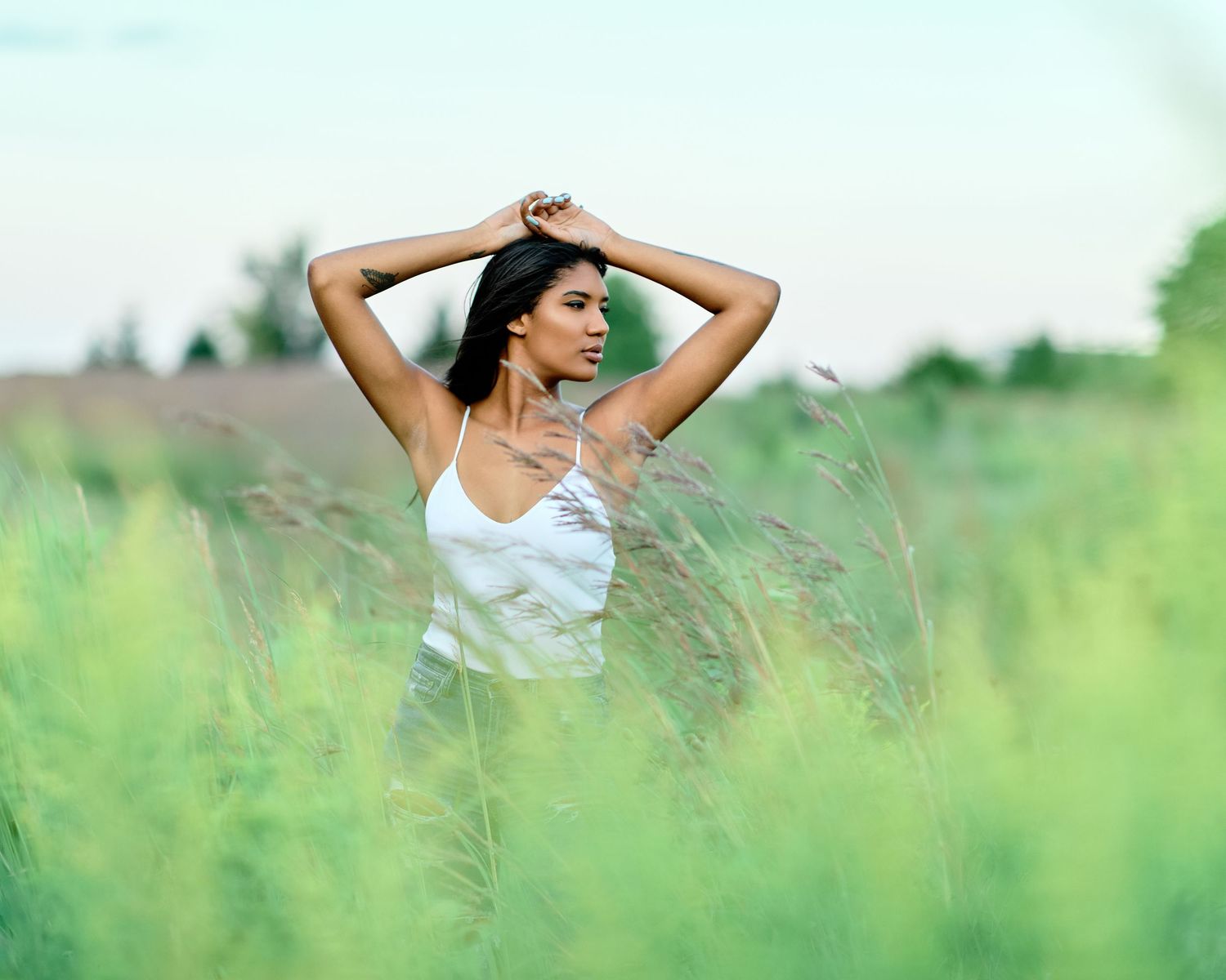Natural light portrait: Woman in white top amid tall grasses, looking aside thoughtfully. Candid style.