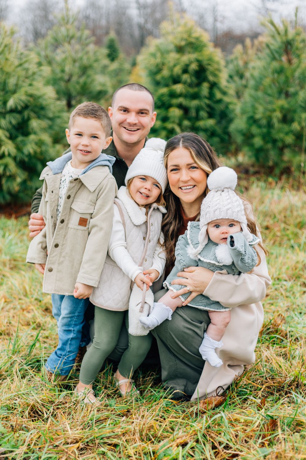 A heartwarming family photo with coordinated outfits standing together in front of evergreen trees.