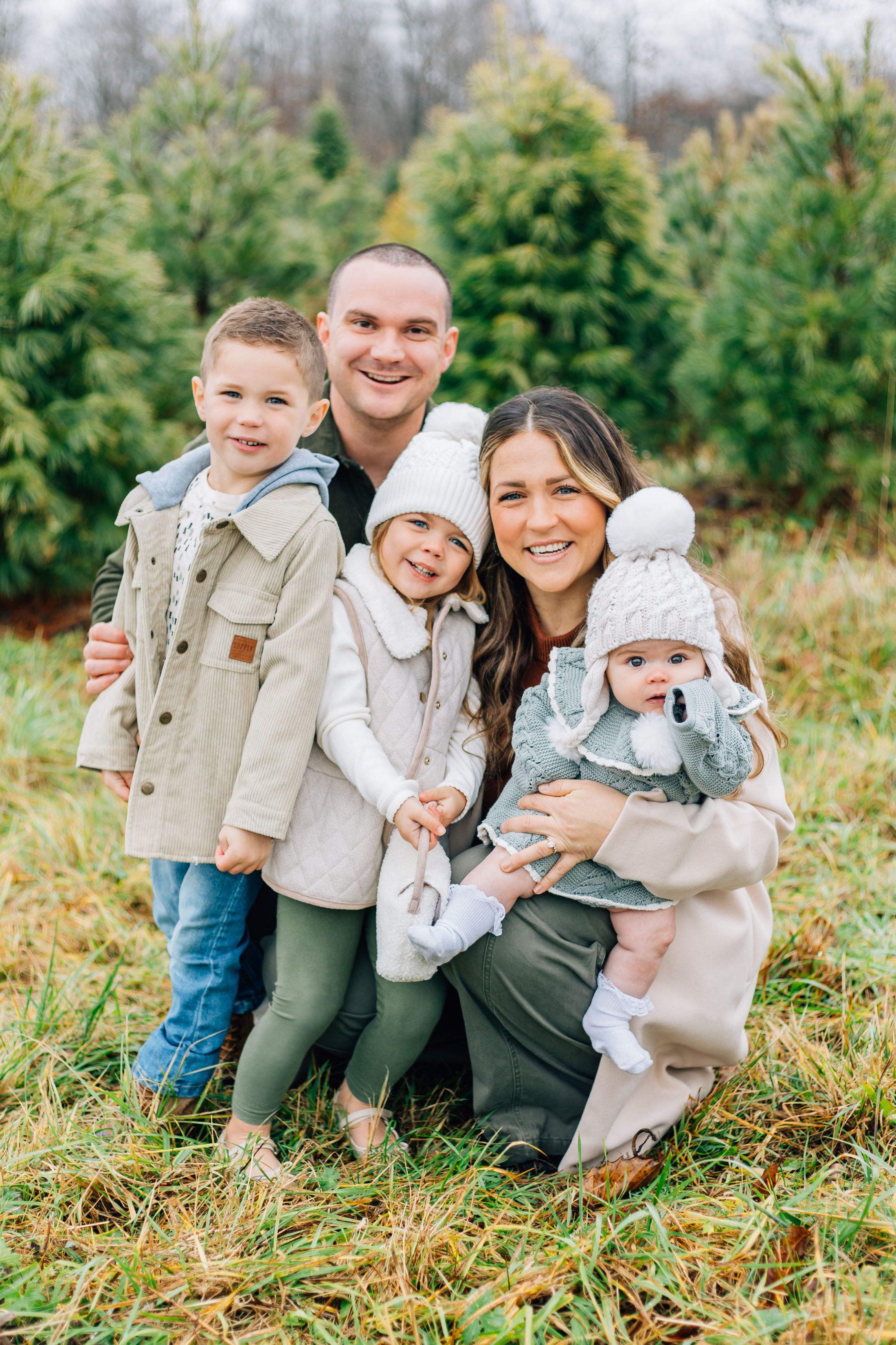 A heartwarming family photo with coordinated outfits standing together in front of evergreen trees.
