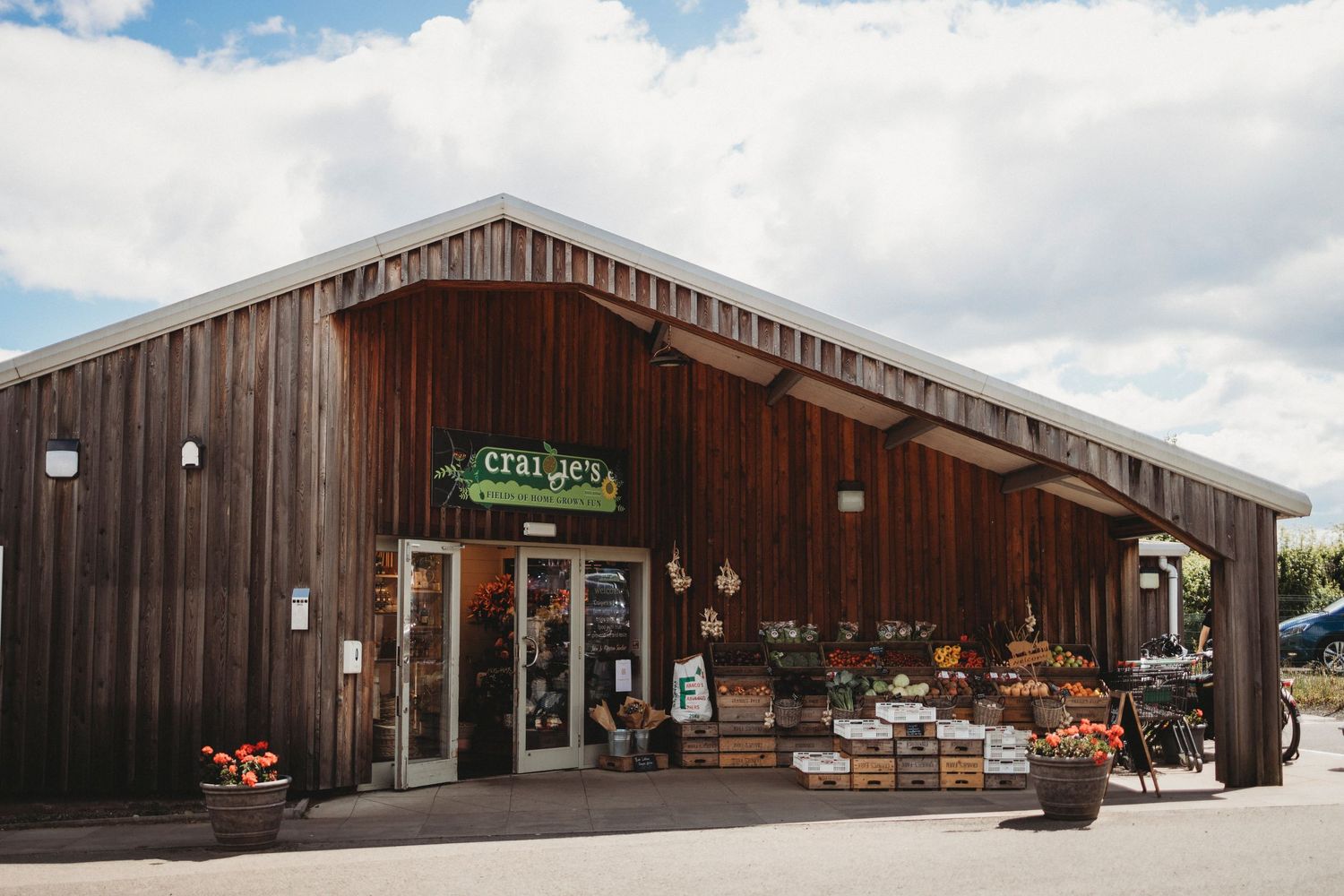Rustic wooden farm store with pumpkins and produce displayed outside under a cloudy sky.