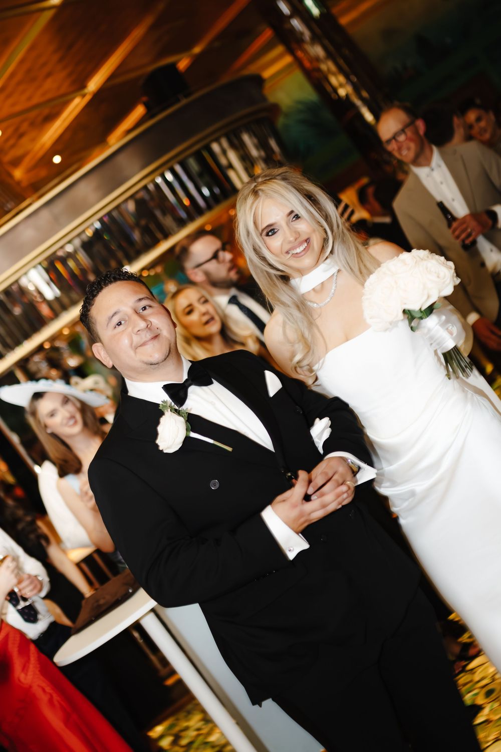 Smiling bride in white gown holding bouquet stands with groom in black tuxedo at elegant wedding reception.
