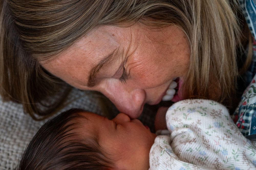Intimate moment captured of mother snuggling newborn baby on textured grey fabric.