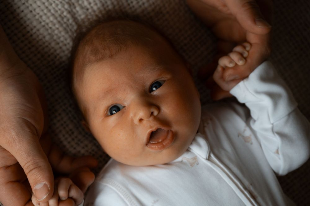 A baby wearing white clothes gazes upward while resting on a textured surface.