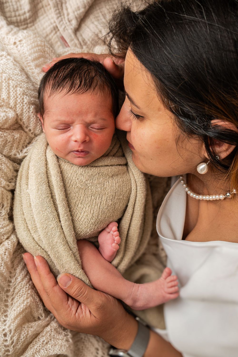 A tender moment between a parent and newborn baby swaddled in beige fabric.