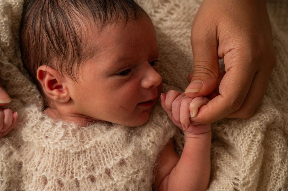 A newborn baby sleeps peacefully on soft cream-colored knit fabric.