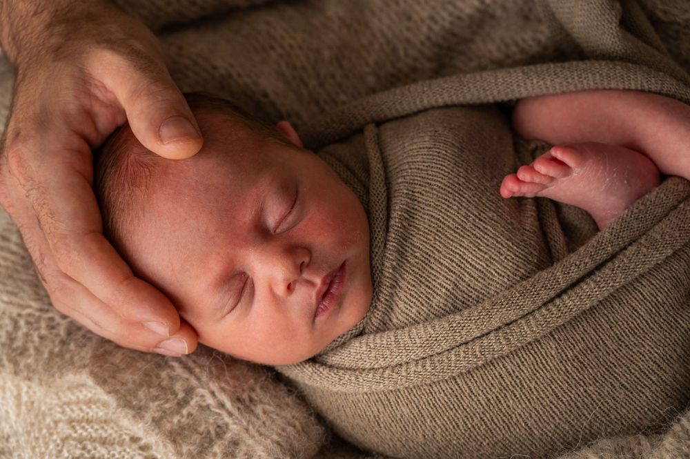 Sleeping newborn baby wrapped in soft brown knit blanket.
