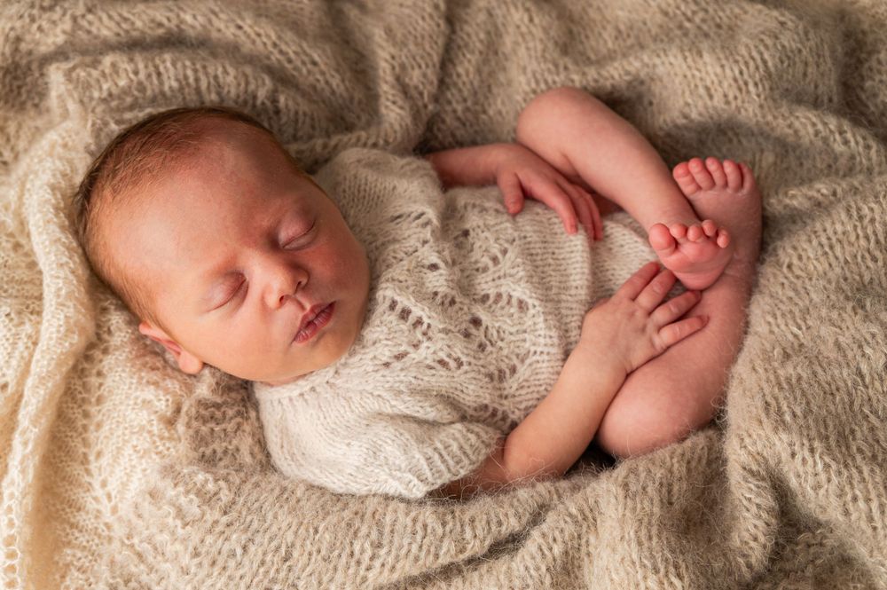 Peaceful newborn baby sleeping in white lace outfit on beige blanket.