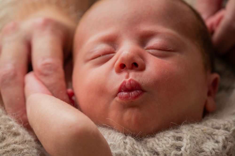 Close up of sleeping newborn baby with pursed lips.
