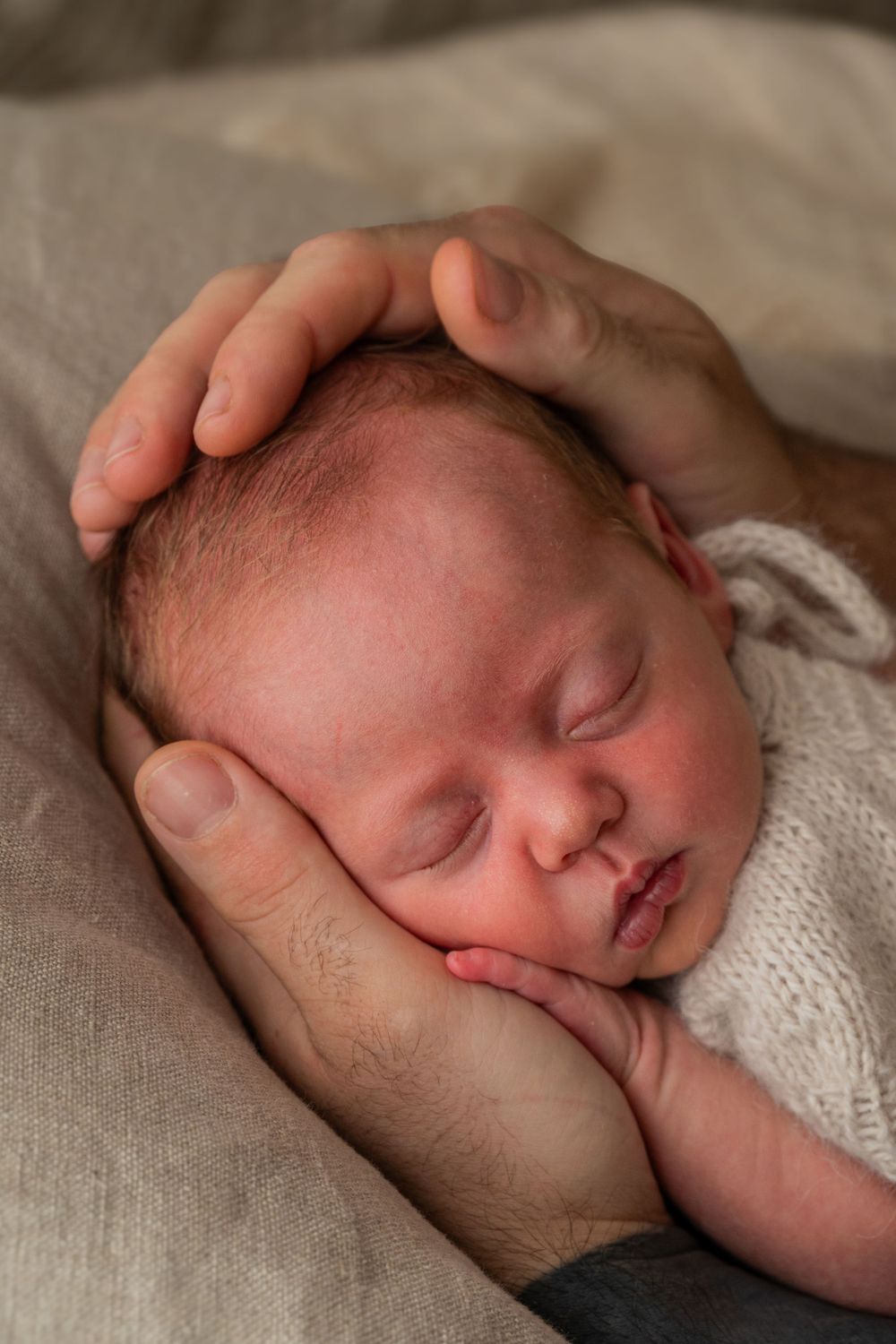 Sleeping newborn cradled in gentle hands on soft blanket.