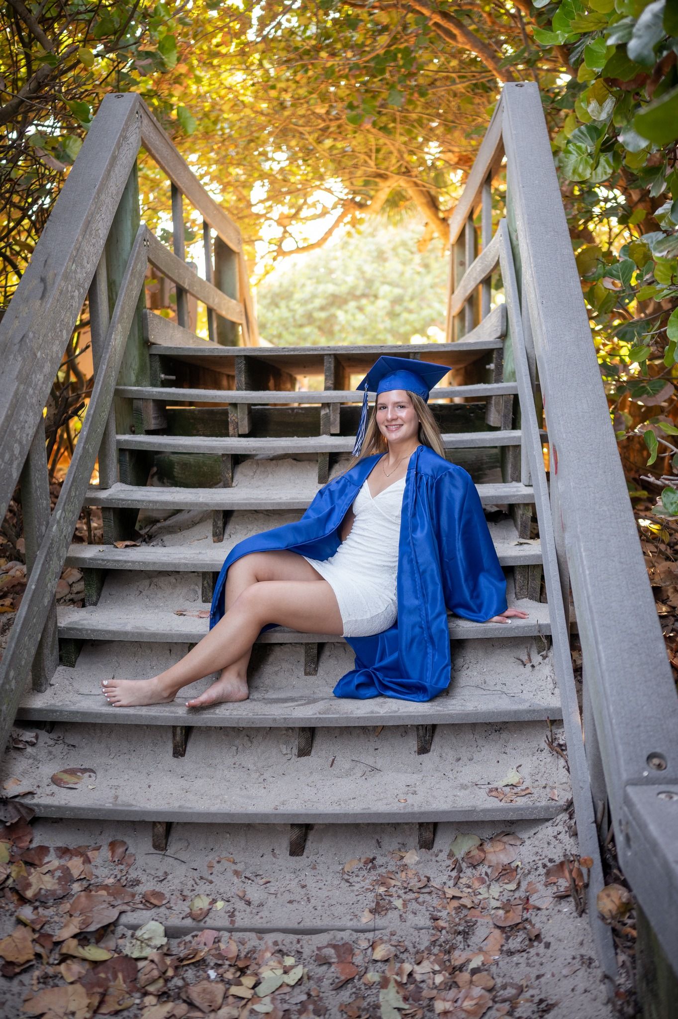Senior girl graduation cap and gown sitting on stairs at beach sunset sand candid moment Melbourne Cocoa Beach Vero Florida Brevard County