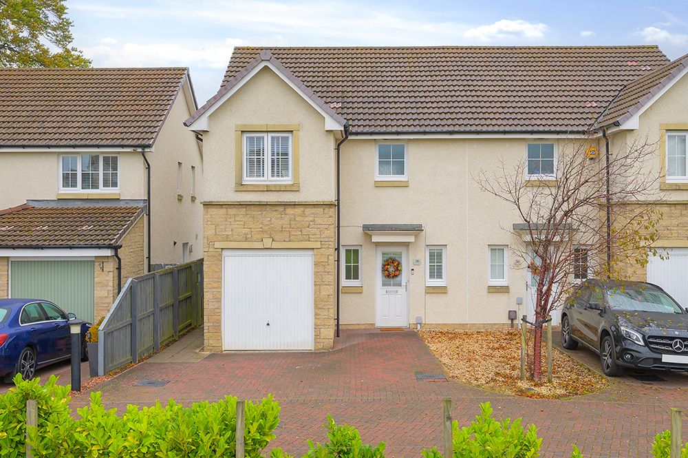 Modern beige detached house with white garage door, paved driveway and landscaped front garden in suburban setting.