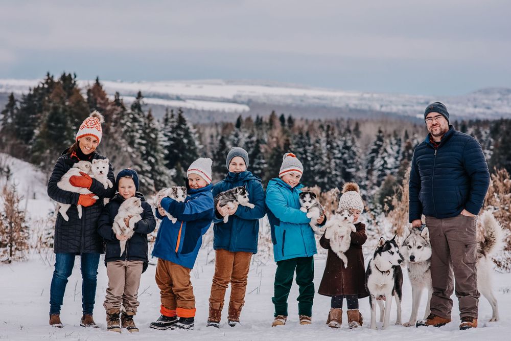 A winter family portrait with dogs against a snowy mountain landscape.