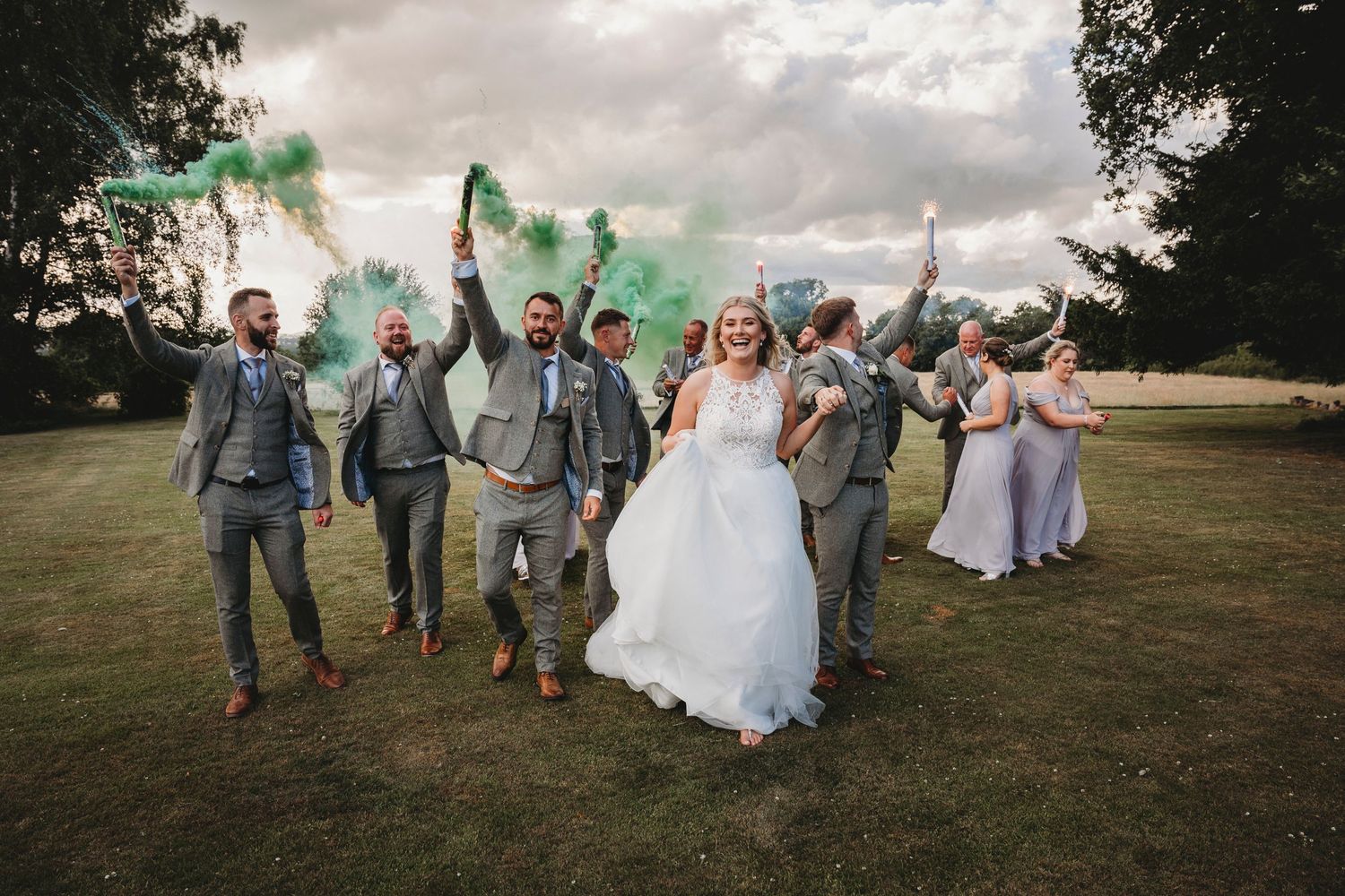 Wedding party jumps joyfully in unison on a grassy hill during sunset celebration.
