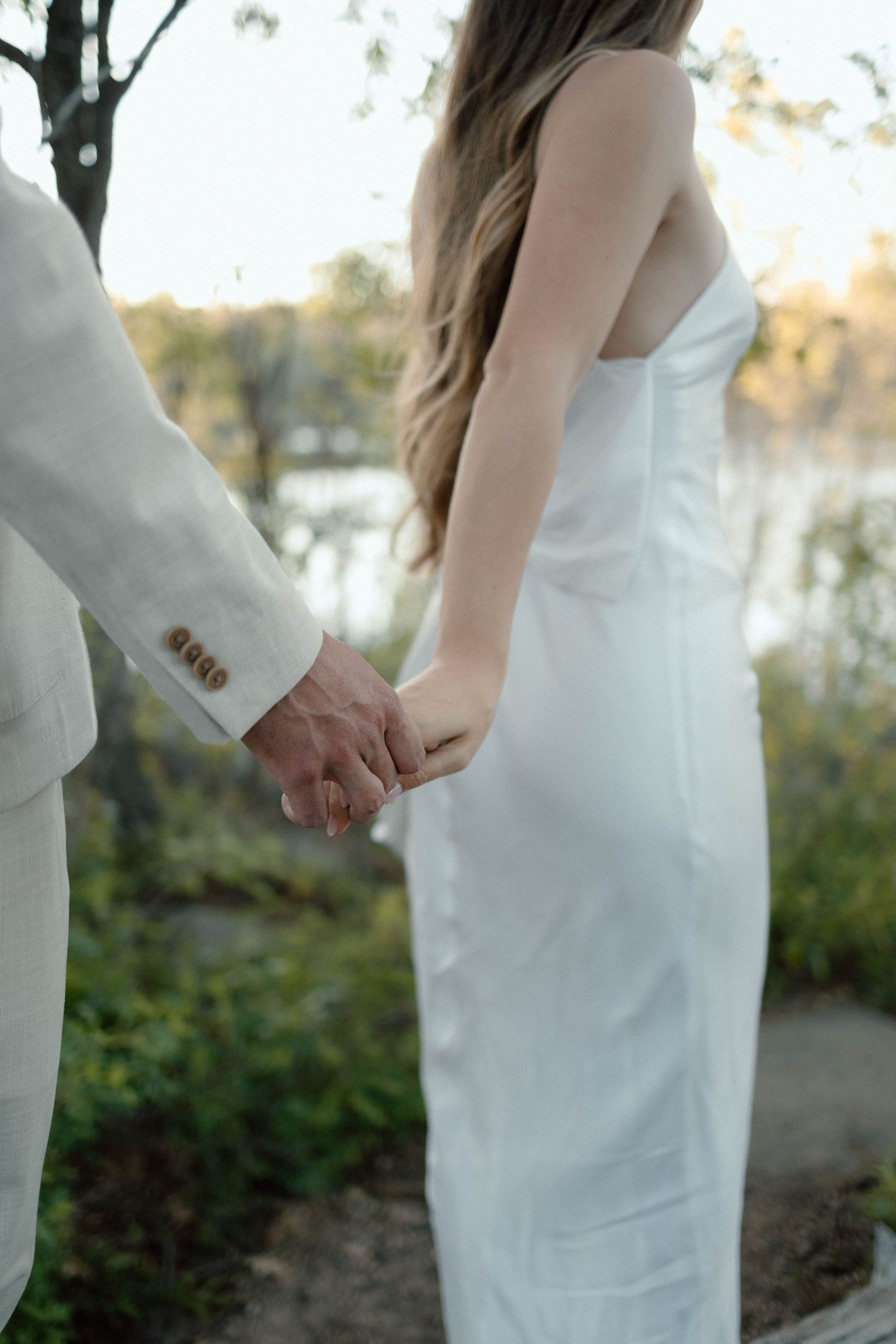 Close up of couple holding hands, with bride in elegant white dress.