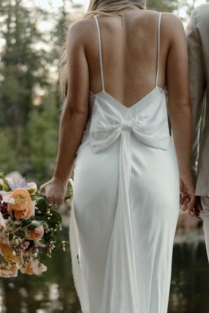 Back view of a sleek white wedding dress with delicate spaghetti straps and an elegant bow detail.