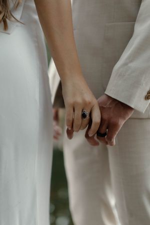 Close-up of hands with a sapphire ring as a couple holds hands in white formal attire.