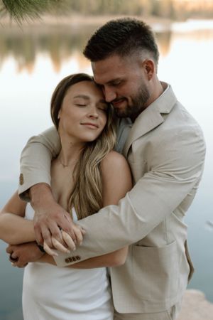 A tender embrace captured against a serene lakeside backdrop at sunset.