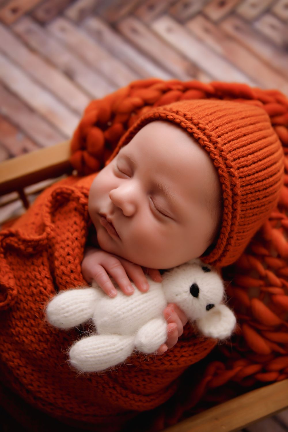 A baby sleeping peacefully in a red knit hat while cuddling a small white stuffed animal.