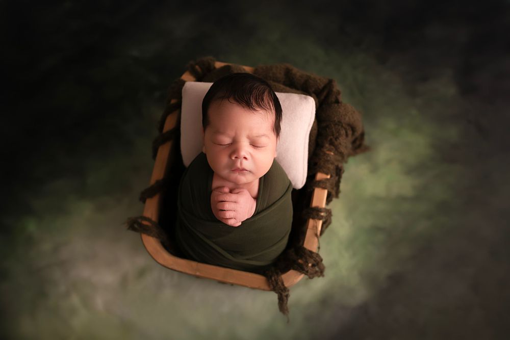 Seven images show a sleeping baby arranged artistically in wooden frames against a dark textured backdrop.