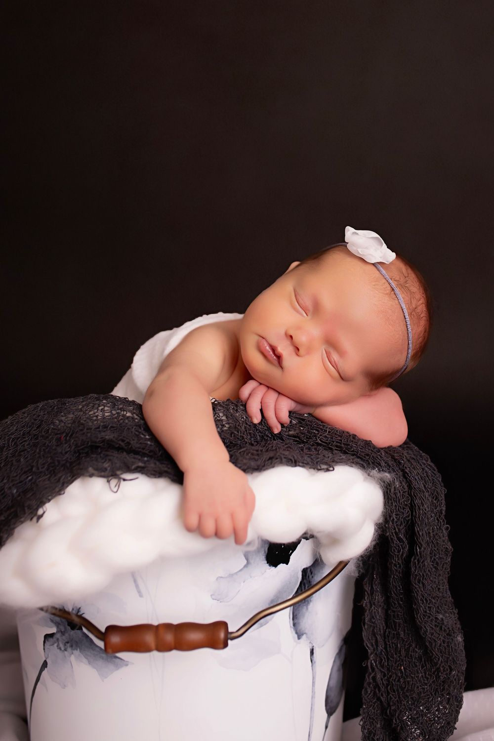 Sleeping newborn peacefully rests on white pillow with dark blanket in professional portrait studio setting.