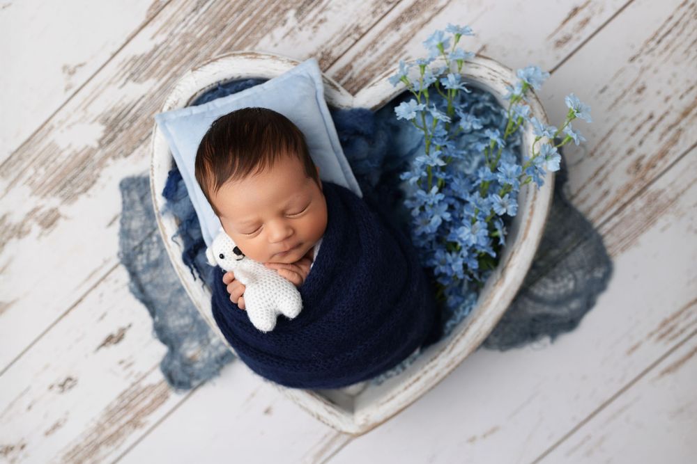 Newborn baby sleeping peacefully in a rustic wooden setting with blue floral decorative elements.