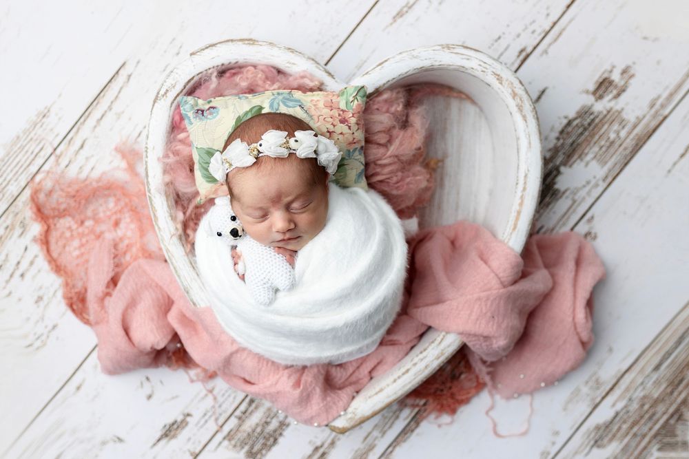 A white ring box with pearls sits on pink fabric against a rustic wooden background.