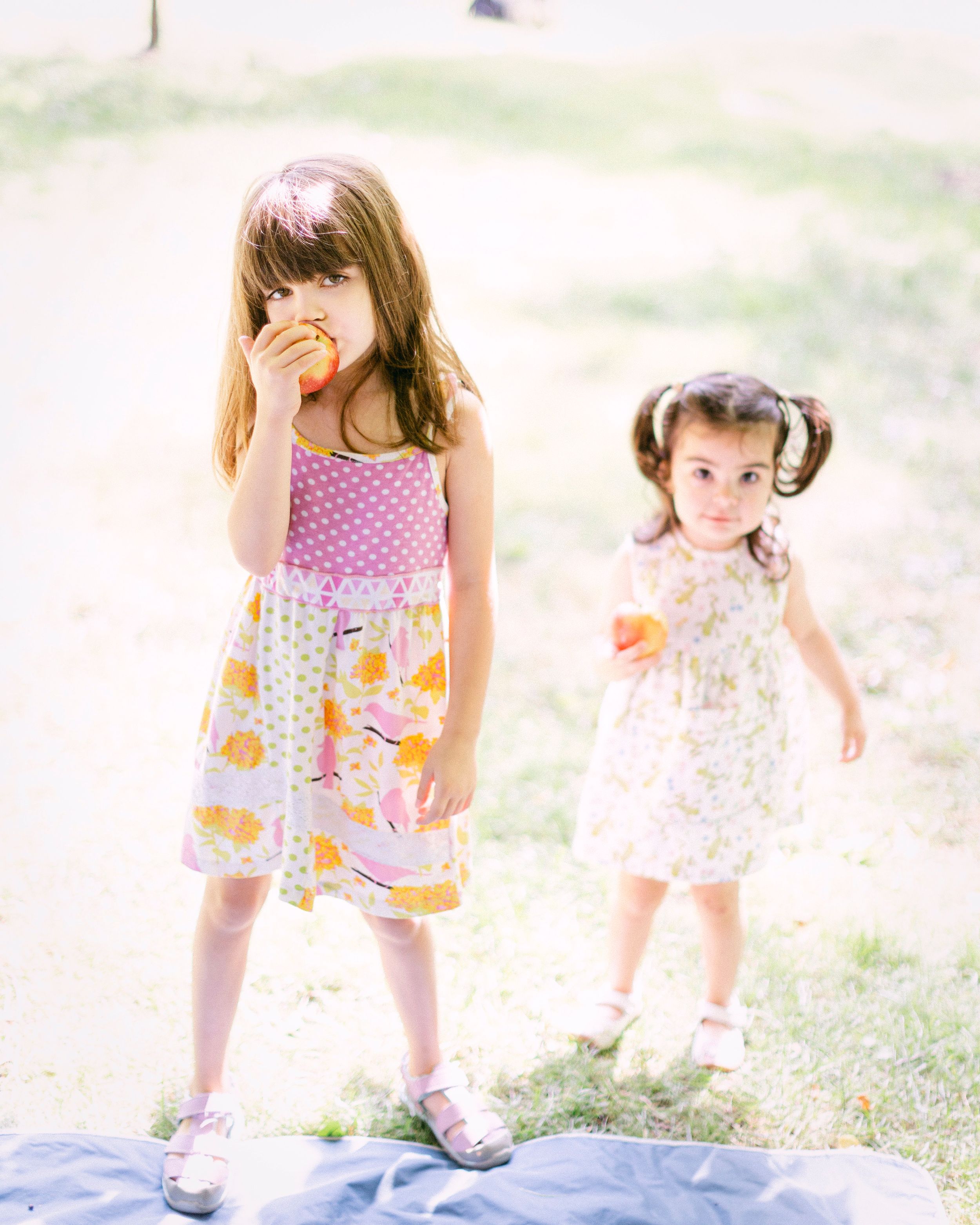 Two children in summer dresses playing outdoors in soft sunlight.