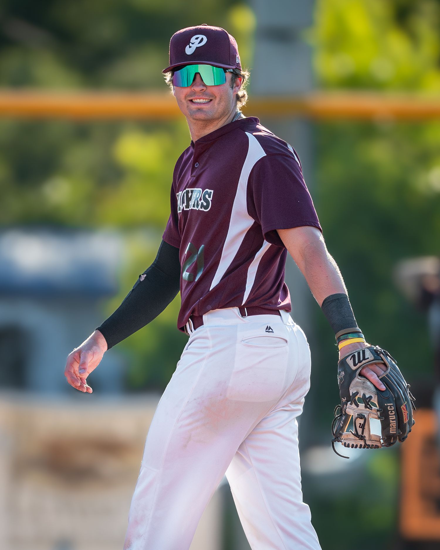 Baseball player in maroon uniform and sunglasses stands ready on field during game.